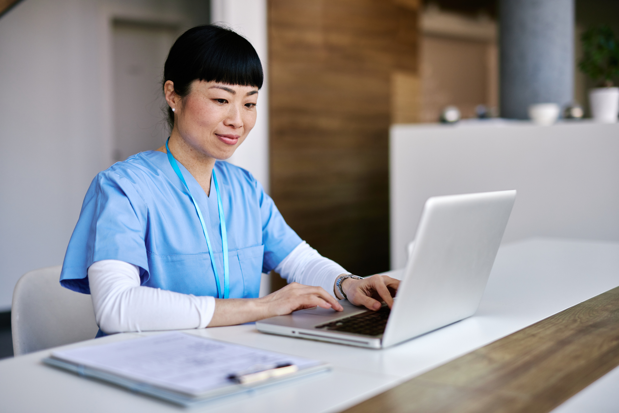 A woman in blue scrubs using a laptop