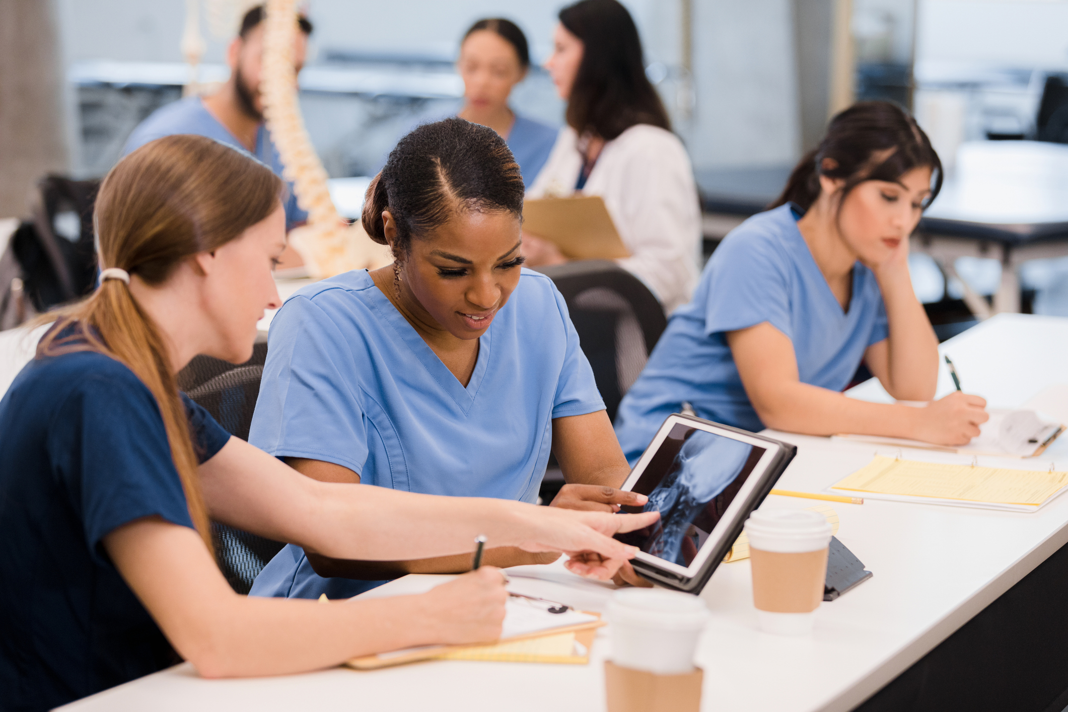 A group of women in scrubs looking at a tablet